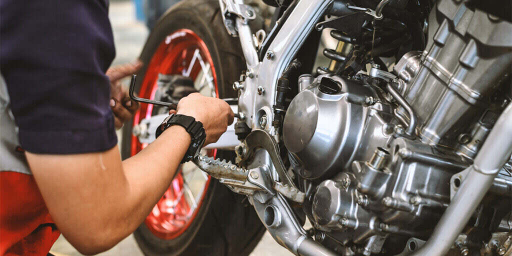 Ein Mechaniker arbeitet an der Reparatur eines Motorrads, konzentriert auf die Einstellung und Wartung der Motor- und Kettenkomponenten.