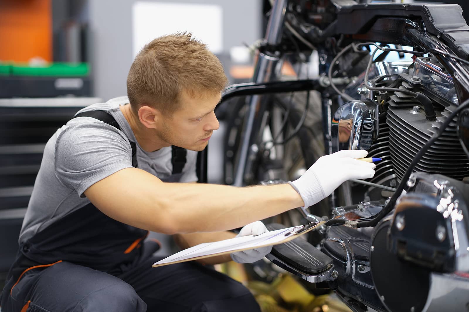 Mechaniker überprüft ein Motorrad in einer Werkstatt und hält ein Klemmbrett in der Hand, für einen Kunden welche einen Technischer Rat benötigt.